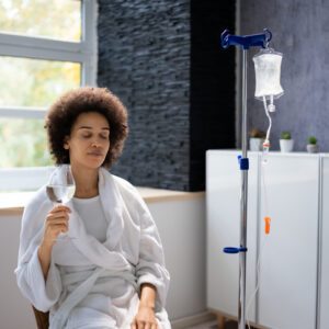 Woman relaxing with IV therapy and drink.